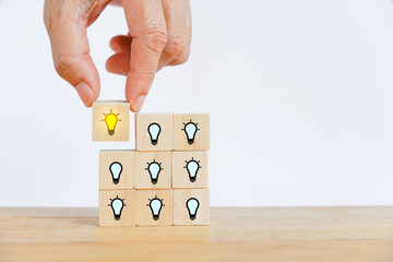 Hand choose the lighten lightbulb icon from stack of wooden block for brainstorming, outstanding, leadership, strategy concept