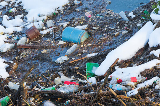 A river in winter, water and snow spoiled with human waste, made of plastic and gas bottles, poisoning environment