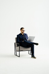 Young smiling businessman sitting in office chair and working on laptop on white background