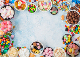Pink lollipop candies in jar with various milk chocolate and jelly gums candies on blue background...