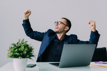 Happy successful young business man cheering with clenched fists in office