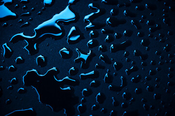 Blau metallisch glänzende Wassertropfen auf schwarzer Textil Oberfläche