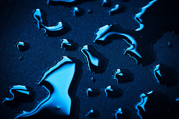 Blau metallisch glänzende Wassertropfen auf schwarzer Textil Oberfläche