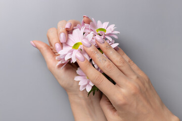 female hands with pink glittering manicure and flowers on gray background. Fashionable trendy female manicure. beauty salon concept. closeup