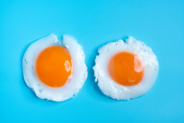 Fried eggs isolated on blue background, top view, soft focus.