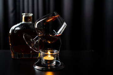 A glass of cognac against the background of a bottle of cognac, an inkwell with a feather on a dark surface