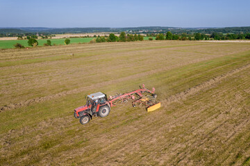 Tractor creates rolls of dry grass, for the subsequent collecting of hay in bales. Preparation of feed for cows.