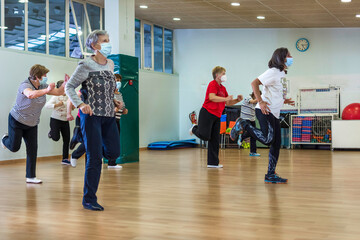 Group of women retired seniors attending gym class. Wearing protective mask, social distancing, Concept of active retirement, fitness. 