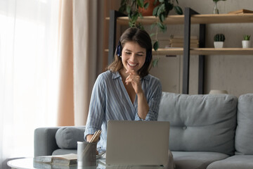 Joyful attractive millennial generation woman in headphones holding video call meeting, studying...