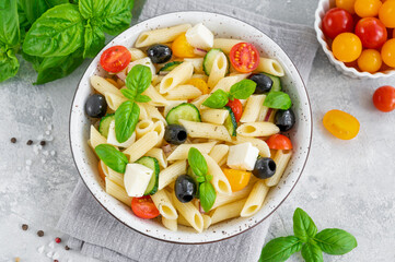 Healthy pasta salad with tomatoes, cucumbers, red onions, olives and cheese in a bowl on a gray background. Copy space.