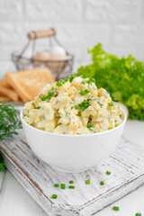 Egg salad with chopped green onions on top in a white bowl for cooking a sandwich on a white wooden background. Selective focus