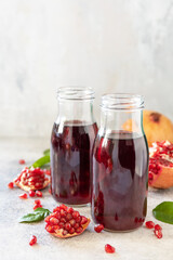 Healthy juicy vitamin drink diet or vegetarian food concept. Pomegranate juice in glass bottles with pomegranates on a light stone tabletop. Copy space.