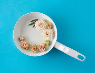 A creative spring summer concept made of a white frying pan and bright bush rose flowers on blue.