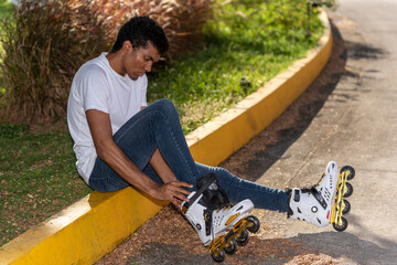 Young latino man sitting putting on inline skates