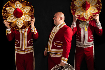 Mexican mariachi musicians cover their faces with a sombrero on a black background. One musician...