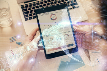 Double exposure of man's hands holding and using a digital device and tech theme hologram drawing....