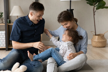Laughing bonding young couple parents tickling happy adorable little kid daughter, having fun...