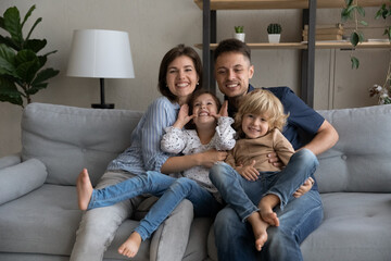 Smiling affectionate young couple parents holding on laps joyful little preschool son daughter...