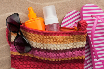 Beach accessories on the sand. Bag, colorful flip flops and bag, sunscreen and sunglasses. Summer vacation. - 482155264
