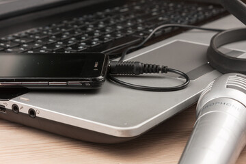 Close-up of a microphone, phone and connected headphones lying on a laptop. Remote work. Office workplace - 482155266