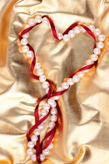 White beads and a red heart-shaped silk ribbon on a golden background - 482155276
