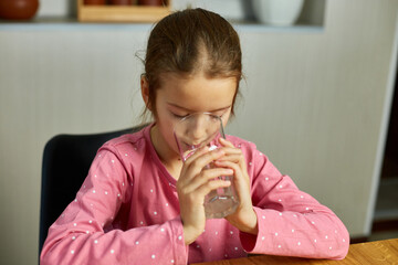 Close up of happy little girl drinking glass fresh water in kitchen