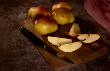 Naklejka na ściany i meble Pears board. Pears and a knife are on a cutting board and one is cut into four parts and the whole composition on a dark background