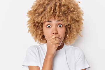 Close up portrait of shocked scared young woman covers mouth with hand stares bugged eyes cannot believe in shocking news dressed casually isolated over white background. Human reaction concept