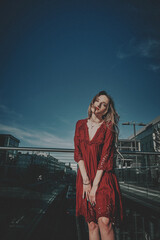 A slender girl with blond long hair in a red dress. Sunny weather girl walks around the city.