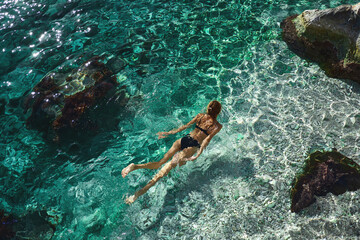 High angle view of woman relaxing in clear water, swimming in turquoise sea over coral reef. Happy island lifestyle. Vacation at Paradise