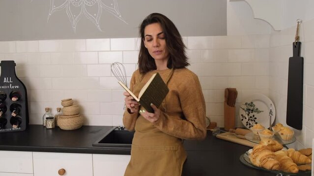 A young woman in the kitchen in an apron rereads recipes, chooses what to cook for dinner 