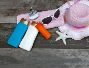 Strandaccessoires: Sonnenbrille mit Hut und Sonnenschutz Produkten  auf einem Holzhintergrund.