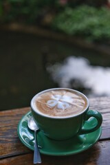 A cup of hot latte or cappuccino topped with latte art or milk foam in a flower shape with green cup and steel spoon