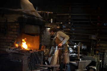 Blacksmith working with open fire in furnace. The blacksmith forging hot iron in workshop