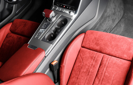 Red luxury modern car Interior. Steering wheel, shift lever and dashboard. Detail of modern red car interior. Automatic gear stick. Part of leather seats with stitching in expensive car