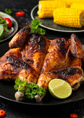 Roast Chicken Tabaka with salad, corn and lime on black plate.