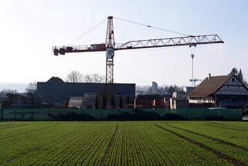 Fototapeta premium Agricultural field in the foreground with construction site in the background on a sunny winter day. Photo taken January 13th, 2022, Zurich, Switzerland.