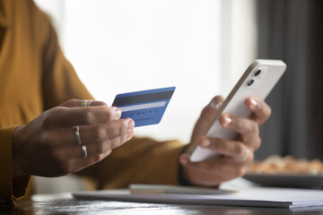 Woman holding smartphone, using credit card, shopping online with ecommerce app, making payment,...