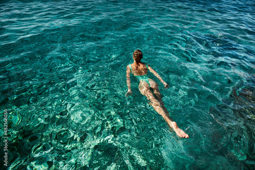 Wall mural top view swimming woman in green swimsuit bikini enjoying in blue sea water, tropical beach destinat