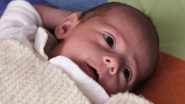 Close up view of a newborn baby looking curious to the side while lying on his back on a bed.