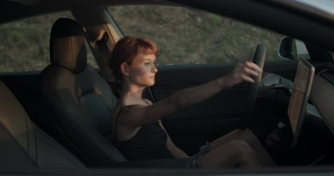 Cute girl in her electric car, using touchscreen controls. Handheld video