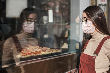 Young asian woman wearing face mask looking at a pizzeria showcase.