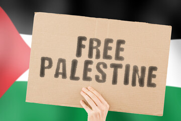 The phrase " Free Palestine " on a banner in men's hand with blurred Palestinian flag on the background. Conflict. War. Dangerous. Security. Safety. Independence. Confrontation