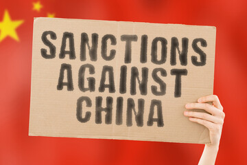 The phrase " Sanctions against China " on a banner in men's hand with blurred Chinese flag on the background. Violation. Ban. Blocking. Violence. Illegal. Freedom. Xinjiang. War. Conflict