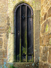 Beautiful historic, aged, wooden arched door set in a stone wall with space for text. The old door with green moss has a keyhole and aged metal door hinges. - 482171806