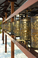 Rows of traditional spinning prayer wheels with tibetan holy sacred mantras at winter temple complex, spiritual asian culture of Hindu and Buddhist faith at local monastery, no people vertical image
