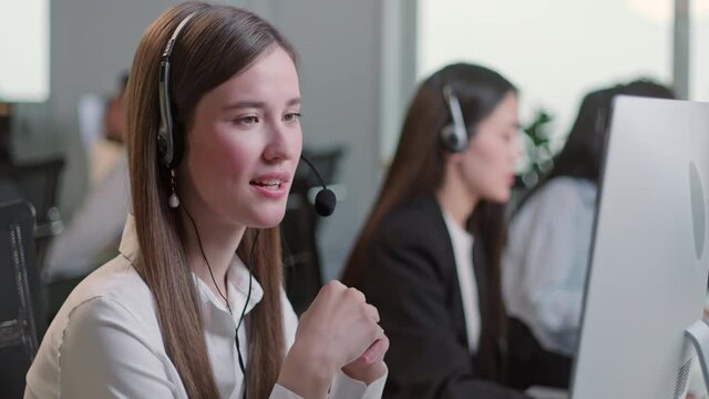 Close Up Portrait of Woman a Technical Customer Support Specialist Talking on a Headset while Working on a Computer in Call center and helpful customer service 24-7. Use desktop pc at computer table