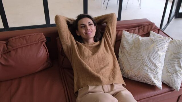 A young woman in the living room on the sofa relaxes, alone, smiles happily, enjoys the moment, music plays in her head in her thoughts 