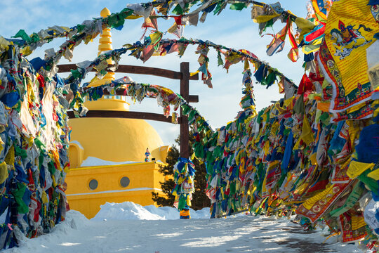 Lots of colorful traditional prayer flags with tibetan mantras hanging out in wind near yellow stupa at snowy temple complex at cold winter, spiritual asian culture at local monastery, no people image