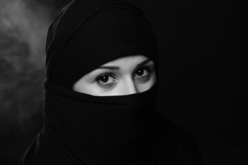 Naklejka premium beautiful oriental girl in a black veil on a black background with smoke close-up portrait 